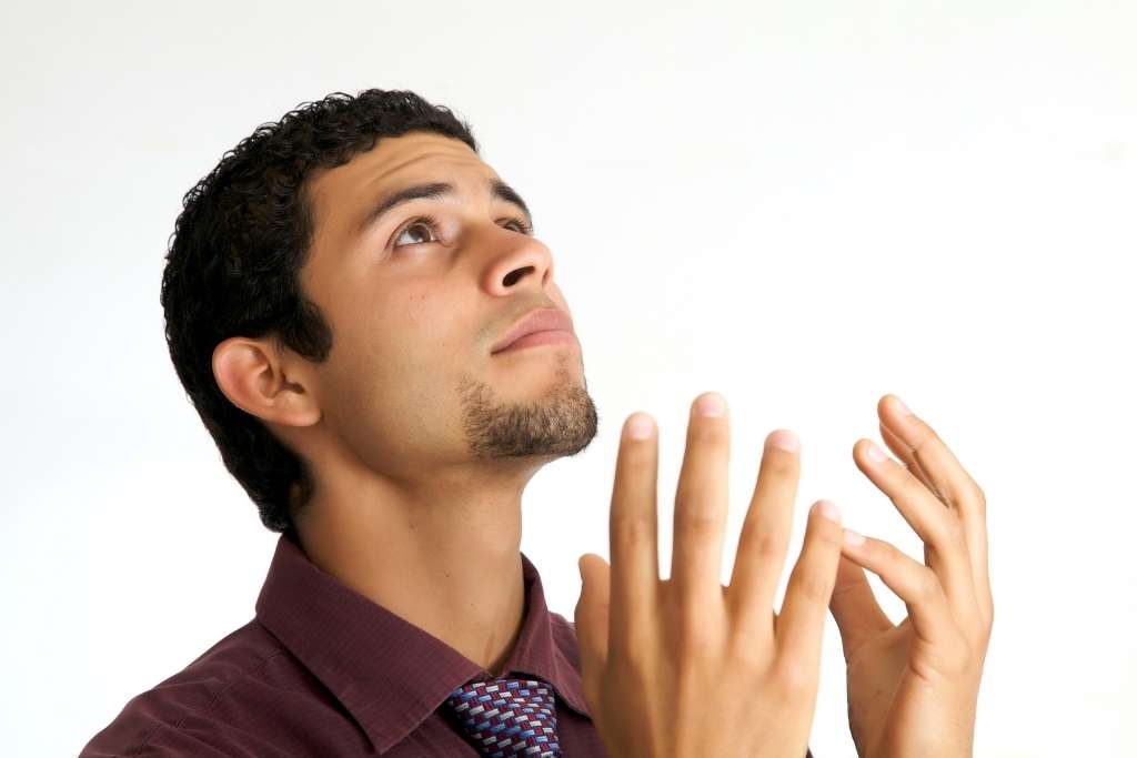 A young man with his hands folded prayerfully staring up towards God.
