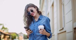 Beautiful woman holding a cup of coffee and using mobile phone outdoors