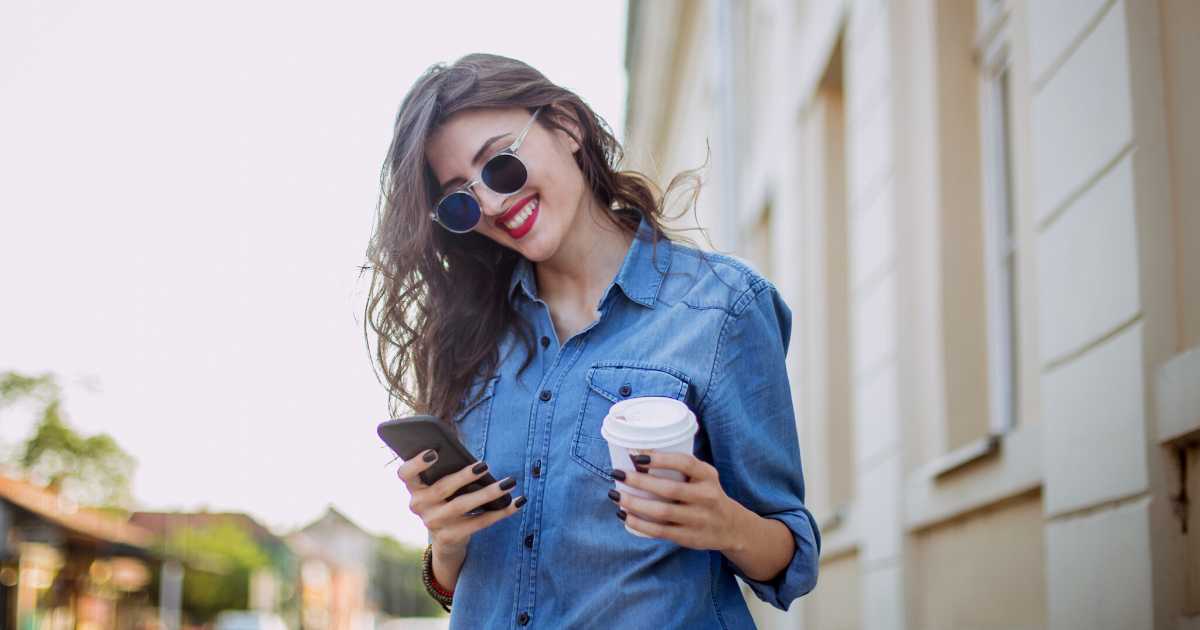 Beautiful woman holding a cup of coffee and using mobile phone outdoors