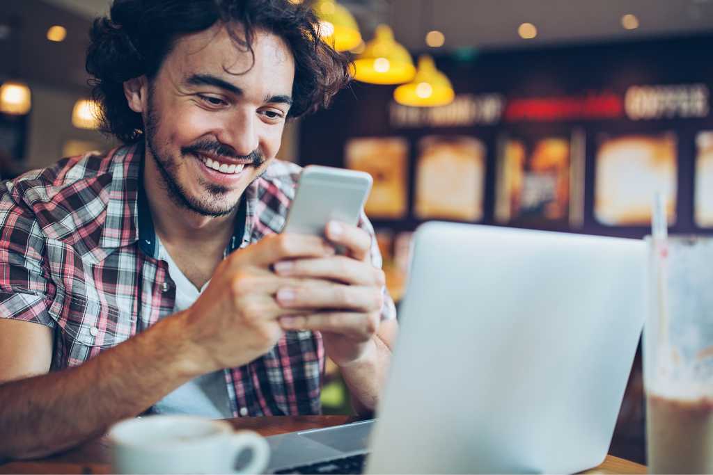 Smiling young man sitting in café and text messaging