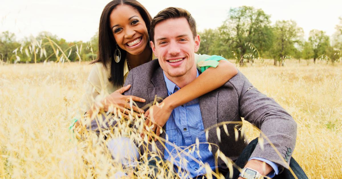 Alternative text: A picture of a young interracial couple sitting on the grass and embracing each other.