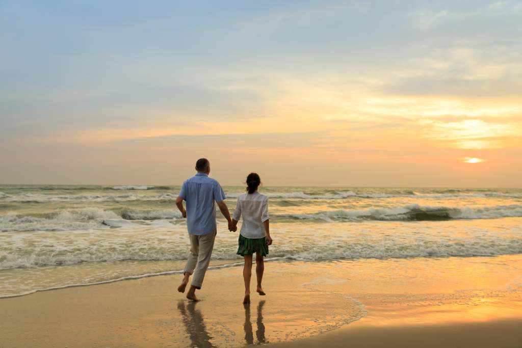 A happy couple walking hand in hand on a beach at sunset, representing the positive and fulfilling nature of healthy relationships, as discussed in the relationship tips provided by Digital Romance Inc.